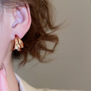 Close-up of golden petal earring with red enamel edge and white pearl on model's ear