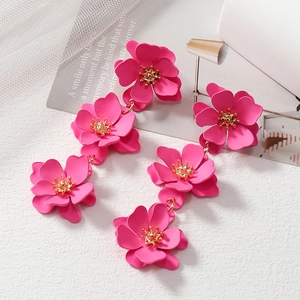 Fashionable long pink flower drop earrings with golden stamens over white textured surface