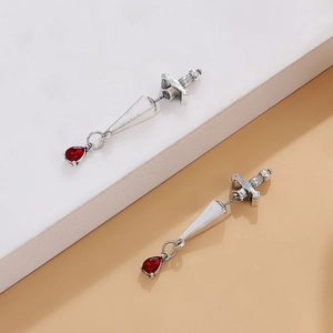 Detail of gothic sword earrings with red teardrop gems on a marble surface