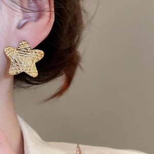 Detailed close-up of a golden star-shaped earring with vintage crinkled metal texture