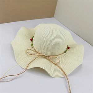 Macro detail of beige straw hat featuring wavy brim and delicate berry flower decor