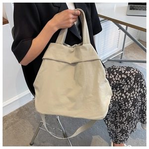 Cream nylon tote bag worn as crossbody showing soft fabric texture and large capacity