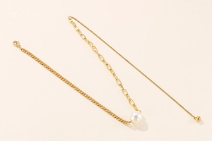 Detail of gold-plated asymmetric chain necklace featuring a large white pearl centerpiece