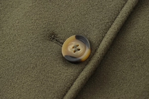 Gros plan sur le tissu en laine vert olive avec détail d'un bouton en écaille