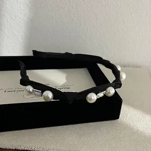 Detail of black fabric headband with pearls and square crystals on a velvet box