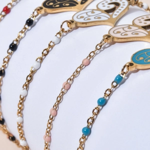 Detail of bohemian gold beaded bracelets with colorful enamel heart and palm pendants