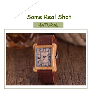 Detail of square natural bamboo watch with Roman numeral dial and brown leather strap