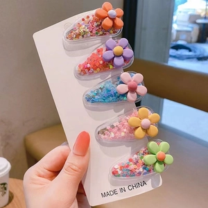 Close-up of five colorful glitter hair clips with floral accents for young girls
