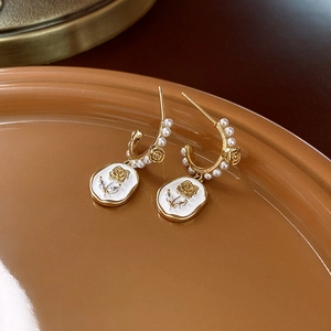 Elegant gold earrings with white enamel rose and pearls, shown from a 45-degree angle