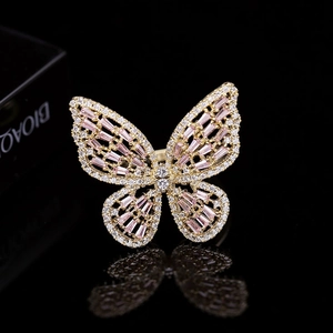 Close-up of golden butterfly ring with pink emerald-cut stones and white zircon details