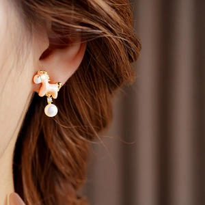 Detail of golden pony earring with white pearl drop and zircon stud worn by model