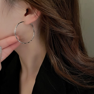 Close-up of model wearing large silver metal hoop earring with polished finish