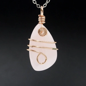 Macro shot of irregular pink rose quartz crystal pendant with rose gold wire wrapping