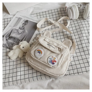 Close-up of a cream canvas messenger bag featuring cute bear ears and cartoon pins