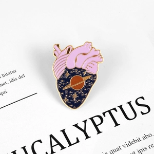 Detailed close-up of a pink heart-shaped enamel pin featuring a starry sky and Saturn