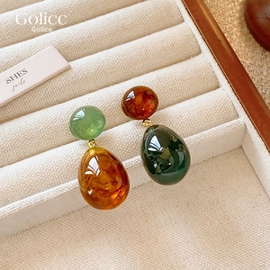 Macro shot of asymmetric resin teardrop earrings with polished amber and green textures