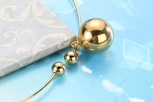 Détail macro d'un bracelet jonc en acier doré avec pendentifs sphériques sur fond bleu