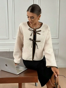 Close-up of beige fleece jacket featuring dark brown trim and elegant bow tie closure