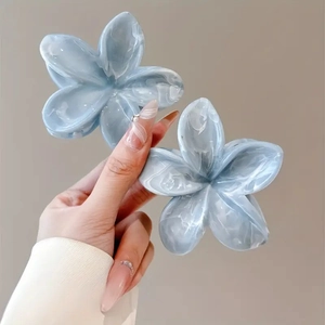 Detail showing two blue marble-textured flower hair claws held against a beige backdrop