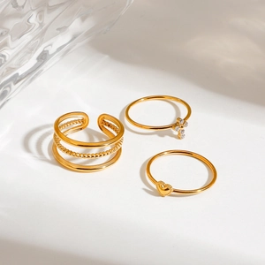 Three-piece gold stainless steel ring set with heart and cross charms on white background