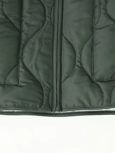 Detail of dark grey-green quilted jacket featuring wave stitching and metal zipper