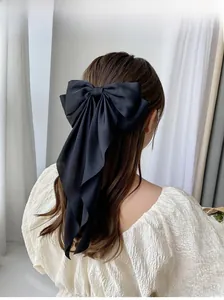 Macro shot of elegant black satin bow hair clip with long ribbons on a wavy ponytail