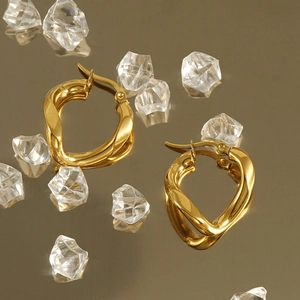 Close-up of gold irregular twisted hoop earrings with a polished mirror finish on ice