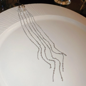 Close-up of elegant silver tassel ear cuff with beads on a ceramic plate