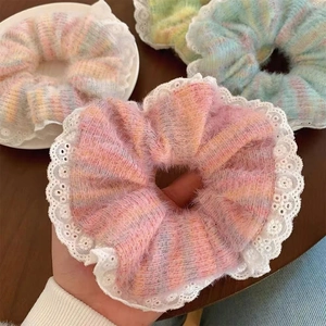 Rainbow knitted scrunchies with white lace trim shown on a wooden table and hand