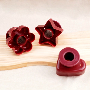 Three-piece set of red plastic donut cutters in flower star and heart shapes on wood