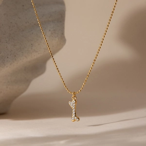 Macro view of gold beaded chain with a crystal-studded bone-shaped pendant on stone