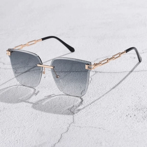 Detail of rimless gradient sunglasses featuring gold metal chain-link temples on a stone surface