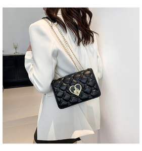 Detail view of black quilted leather shoulder bag with golden heart emblem and chain strap