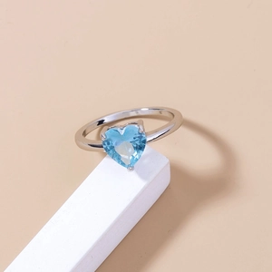 Close-up of heart-shaped blue gemstone ring on a white geometric display stand