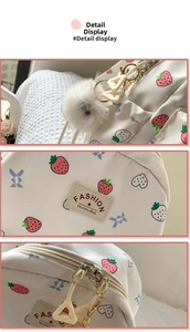 Detail view of strawberry print backpack featuring white pompom and fashion mummy bag label