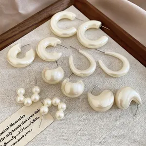 Elegant acrylic drop earring set in cream white and pearl tones on a beige linen background