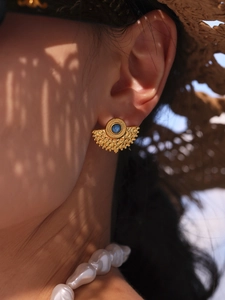 Detailed close-up of vintage gold fan-shaped earrings with blue beads on female model