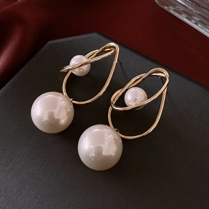 Detailed close-up of geometric gold metal earrings with dual pearls on dark background