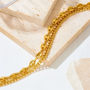 Gold double-layered bracelet with coffee bean and Cuban links on a minimalist stone backdrop
