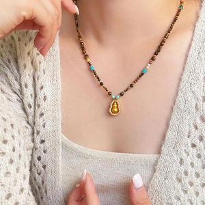 Ethnic gourd necklace with tiger eye stones and zircons worn on a beige knit sweater
