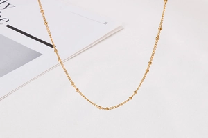 Detailed close-up of a golden stainless steel bead chain necklace on a white surface