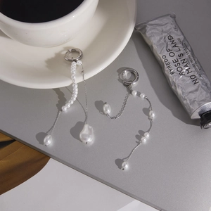 Detailed shot of asymmetrical stainless steel pearl tassel earrings on a sleek surface