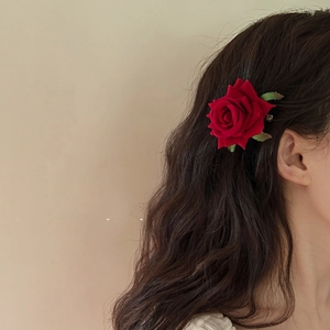Detailed close-up of a large red silk rose hair clip with green leaves on model's hair