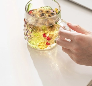 Detailed close-up of a hand-painted glass mug featuring embossed grape and floral patterns