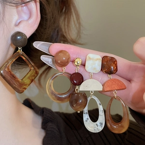 Detail of geometric resin and wood earrings in earthy tones held to show fine texture