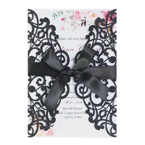 Detail of laser-cut wedding invitation with black glitter cover and satin bow decoration