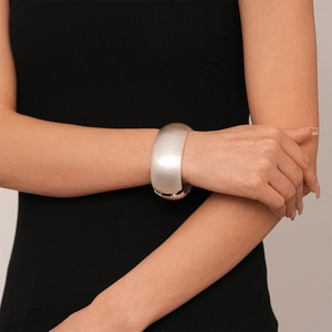 Close-up of a wide brushed silver metal cuff bracelet on a model's wrist with black knitwear