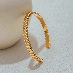 Detailed macro view of a golden stainless steel cuff bracelet with sculptural ribbed texture