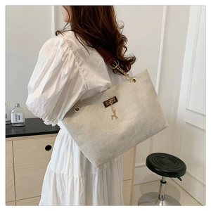 Detail of cream canvas tote bag featuring gold deer charm and leather chain strap