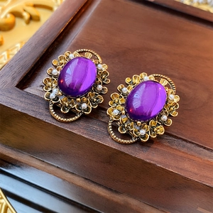 Close-up of vintage gold clip earrings with purple oval gems and white pearl floral details